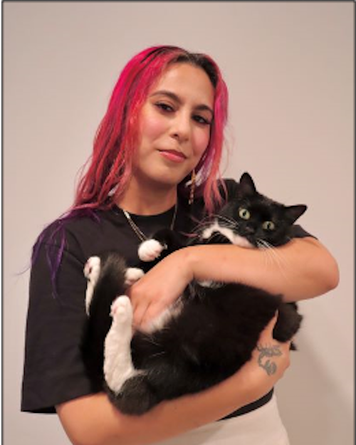 Person with long pink hair holding a black and white cat.
